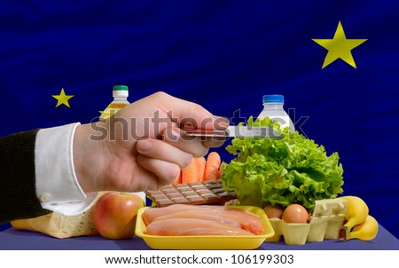 man stretching out credit card to buy food in front of complete wavy american state flag of alaska