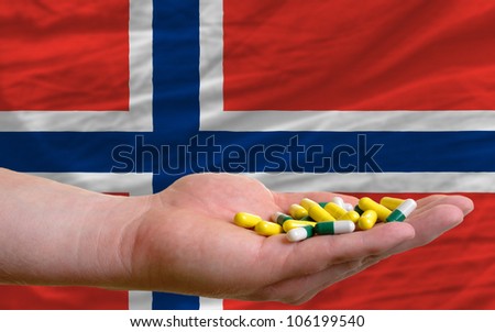 man holding capsules in front of complete wavy national flag of norway symbolizing health, medicine, cure, vitamins and healthy life