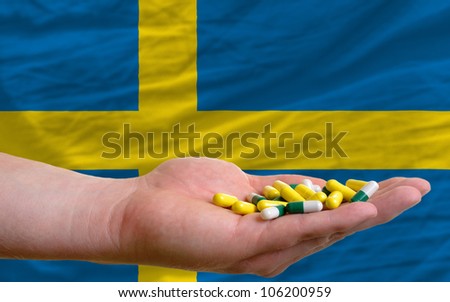 man holding capsules in front of complete wavy national flag of sweden symbolizing health, medicine, cure, vitamins and healthy life