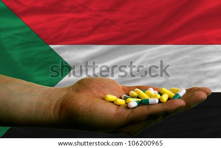 man holding capsules in front of complete wavy national flag of sudan symbolizing health, medicine, cure, vitamins and healthy life