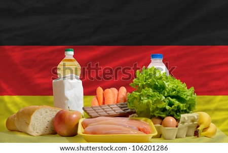 complete national flag of germany covers whole frame, waved, crunched and very natural looking. In front plan are fundamental food ingredients for consumers, symbolizing consumerism