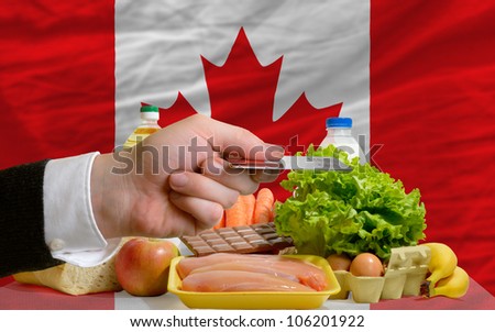 man stretching out credit card to buy food in front of complete wavy national flag of canada