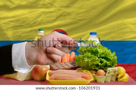 man stretching out credit card to buy food in front of complete wavy national flag of colombia