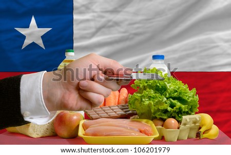 man stretching out credit card to buy food in front of complete wavy national flag of chile