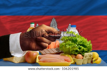 man stretching out credit card to buy food in front of complete wavy national flag of cambodia
