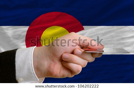 man stretching out credit card to buy goods in front of complete wavy national flag of american state of colorado