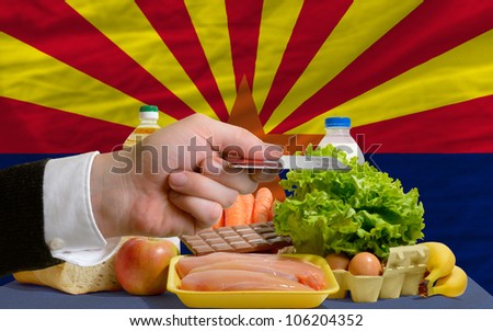 man stretching out credit card to buy food in front of complete wavy american state flag of arizona