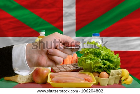 man stretching out credit card to buy food in front of complete wavy national flag of basque