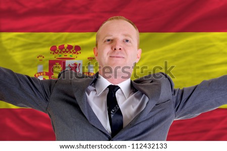 joyful investor spreading arms after good business investment in spain, in front of flag