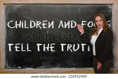 Successful, beautiful and confident woman showing Children and fools tell the truth on blackboard
