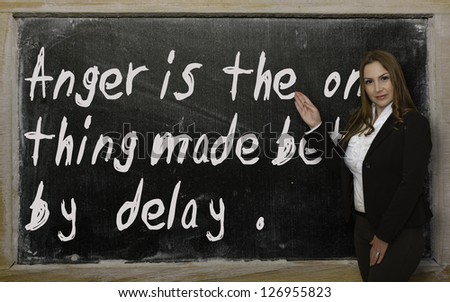 Successful, beautiful and confident woman showing Anger is the one thing made better by delay on blackboard