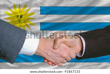 two businessmen shaking hands after good business investment  agreement in uruguay, in front of flag
