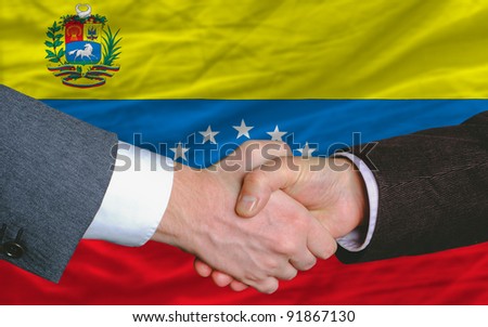 two businessmen shaking hands after good business investment  agreement in venezuela, in front of flag