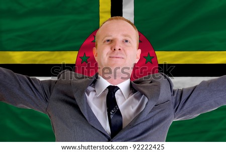 joyful investor spreading arms after good business investment in dominica, in front of flag