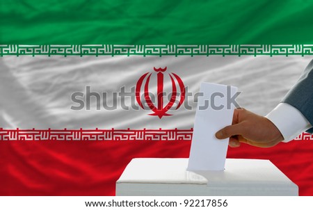 man putting ballot in a box during elections in iran in front of flag