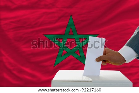 man putting ballot in a box during elections in morocco in front of flag