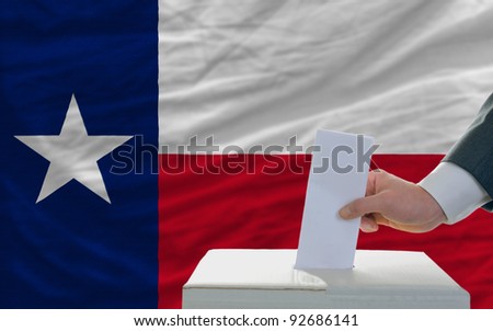 man putting ballot in a box during elections  in front of flag american state of texas