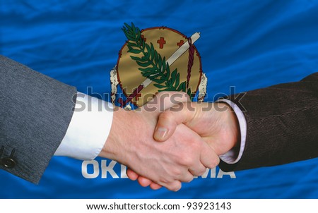 two businessmen shaking hands after good business investment agreement in front US state flag of oklahoma