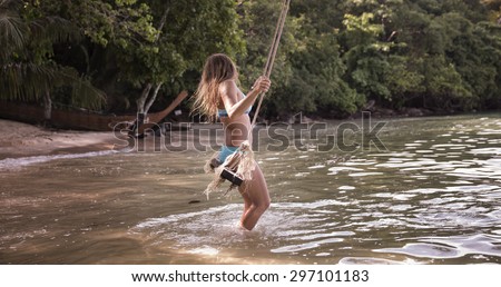 Adult Caucasian woman in blue swimsuit swinging on a rope swings by the beach.