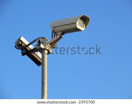 Two surveillance cams on top of a pole, seen from below against a blue sky