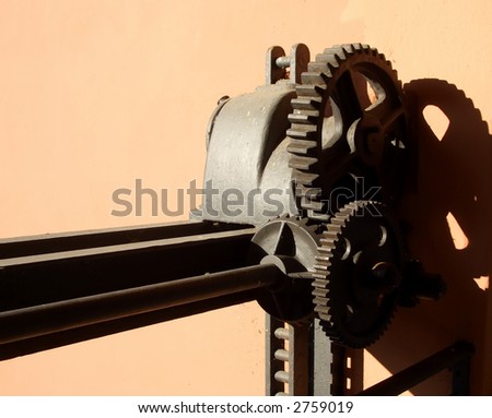 Old rusted watergate gears against brown wall casting strong shadows