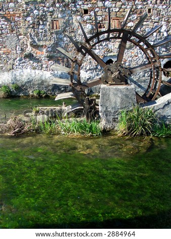 Antique rusted watermill wheel and green water river