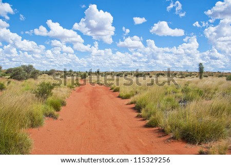 Unsealed dirt road with typical red sand leading through the outback of the red center of Australia