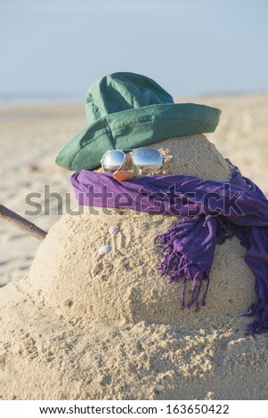 Snowman on beach with shells as mouth, sun glasses,hat and scarf