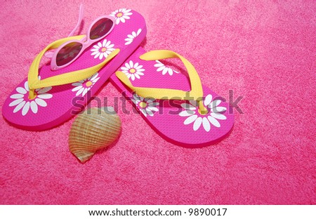 Pretty pink flip flop sandals, sunglasses, and seashell on pink beach towel