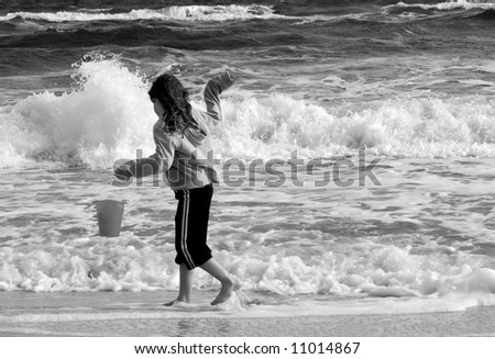 Young girl at beach during rough surf holding shell collection pail