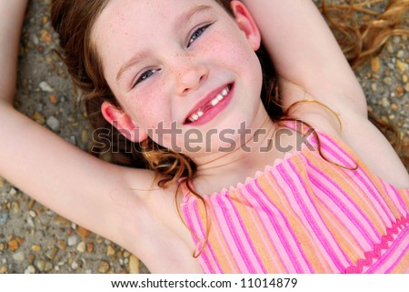Cute girl with missing front tooth laying outside on ground, relaxing