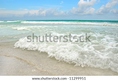 Gentle waves of beautiful ocean crashing onto beach under pretty sky