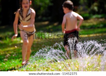 Young girl and boy playing in outdoor yard sprinkler