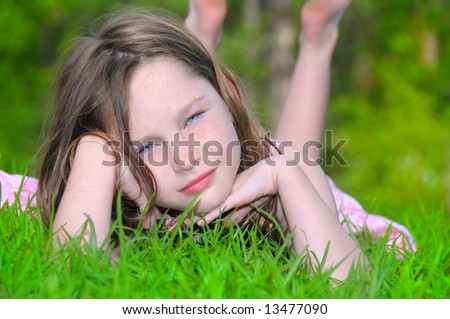 Pretty young girl laying on grass outside in summer