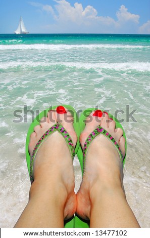 Feet in Flip Flop Sandals at Seashore with Sailboat in Distance