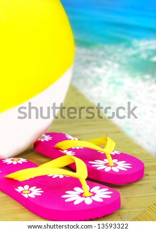 Colorful flipflop sandals and inflatable beach ball by ocean