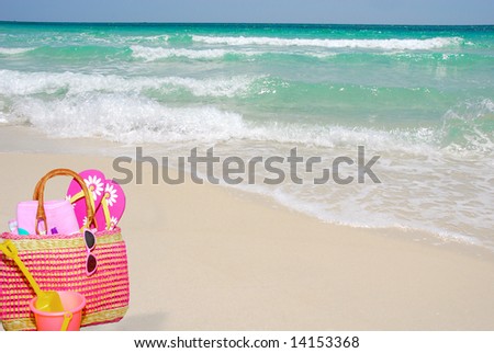 Pretty pink beach bag and accessories on sand by ocean