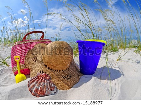 Straw beach bag and hat by sand toys on dune