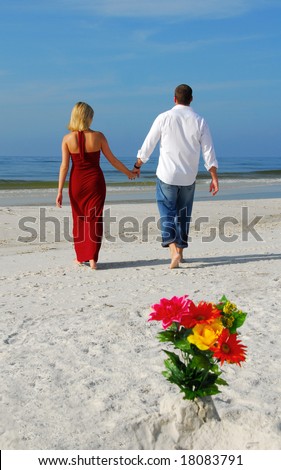 Romantic couple walking away from bouquet in beach sand