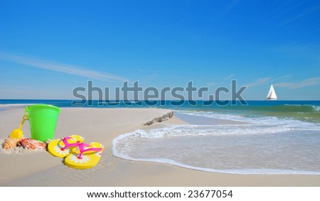 Pretty beach sand toys on dune with gentle waves with sailboat in distance under blue sky