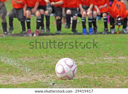 Soccer ball on field with childhood team on bench in distance