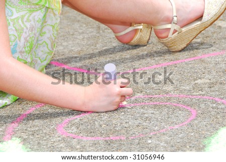 Young girl on sidewalk drawing chalk art on ground