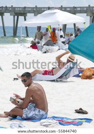 PENSACOLA BEACH - JUNE 23: Beachgoers rest on the beach on June 23, 2010 in Pensacola Beach, FL. BP oil workers are seen in the background.