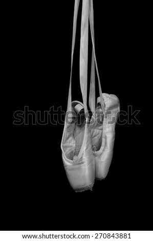 Black and white ballet pointe shoes hanging from ribbons with black background