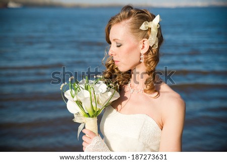 Beautiful bride with a bouquet of calla lilies on coast of river in summer. Professional make-up and hairstyle.