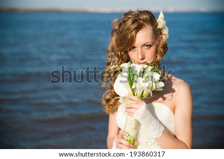Beautiful bride with a bouquet of calla lilies on coast of river in summer. Professional make-up and hairstyle.