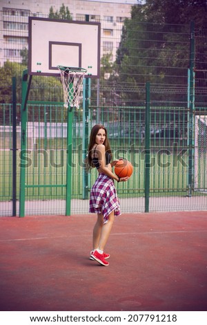 Beautiful young woman playing basketball outdoors.  The girl on the sports ground