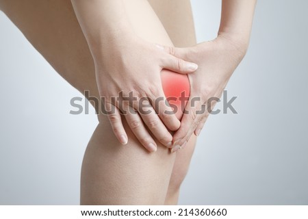 Knee pain of the woman on gray background.  Red dot.