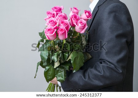 Man in suit with bouquet of roses. Pink flowers on a gray background
