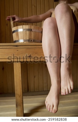 Beautiful female legs in sauna, bath accessories. Wooden bucket and sticks